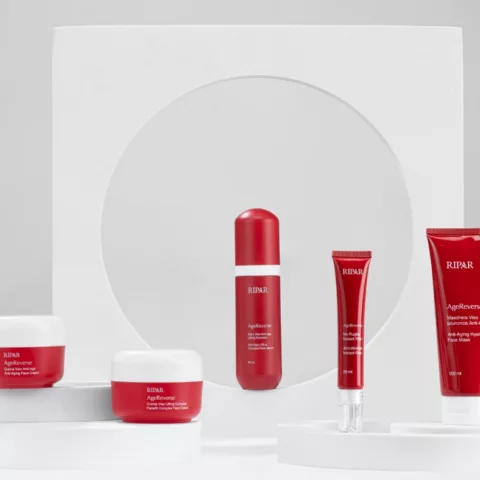 La visual identity di prodotti cosmetici Ripar AgeReverse, caratterizzati da confezioni rosse e bianche, esposti su una disposizione geometrica bianca. I prodotti includono creme viso, sieri e maschere anti-età, progettati per il trattamento della pelle.