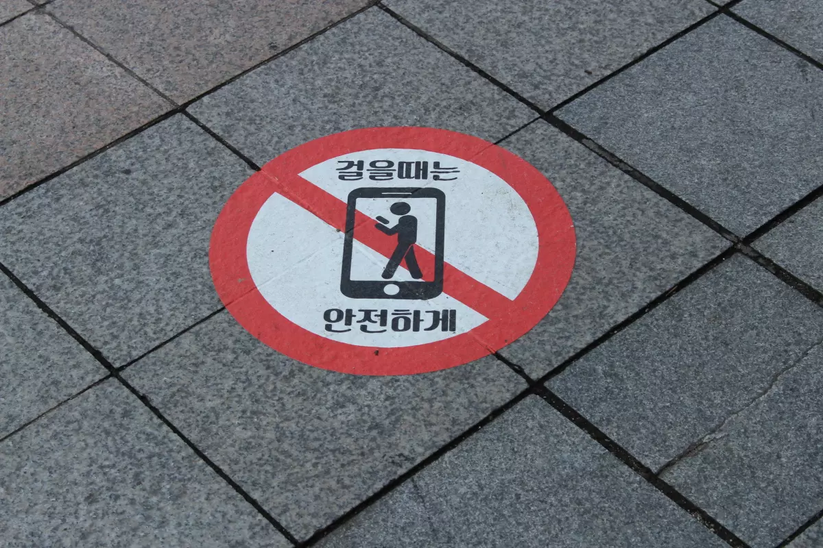 Segnale orizzontale su marciapiede in Corea che vieta l’uso dello smartphone mentre si cammina, con pittogramma e scritte coreane.