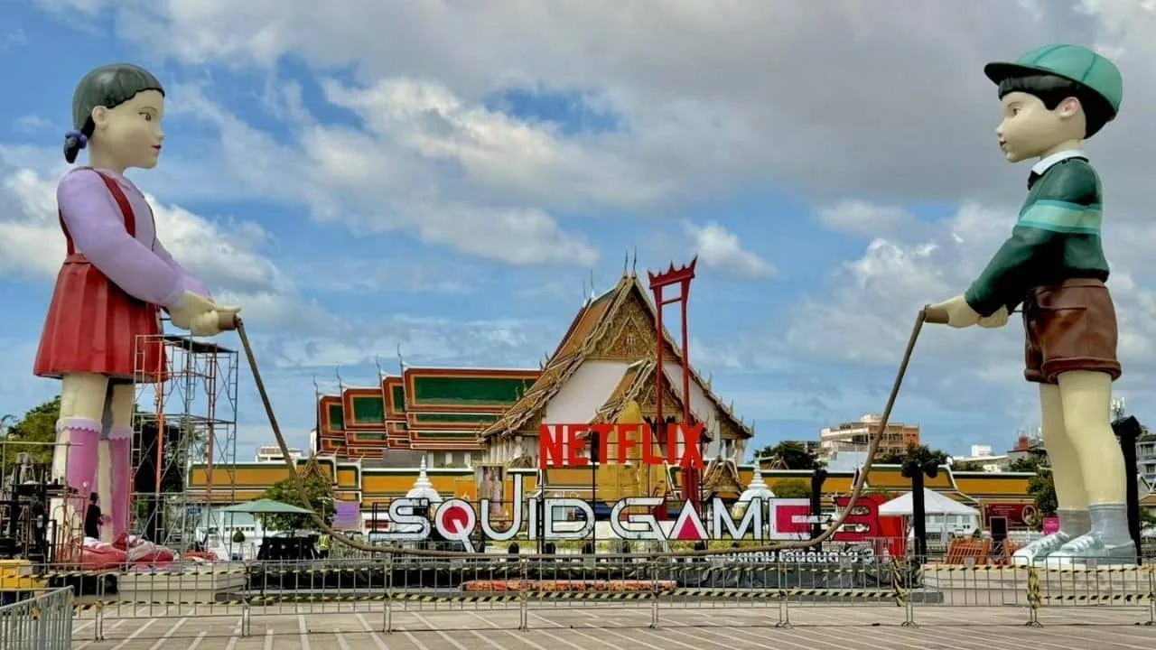 Statue giganti delle bambole di Squid Game davanti a un tempio a Bangkok con logo Netflix
