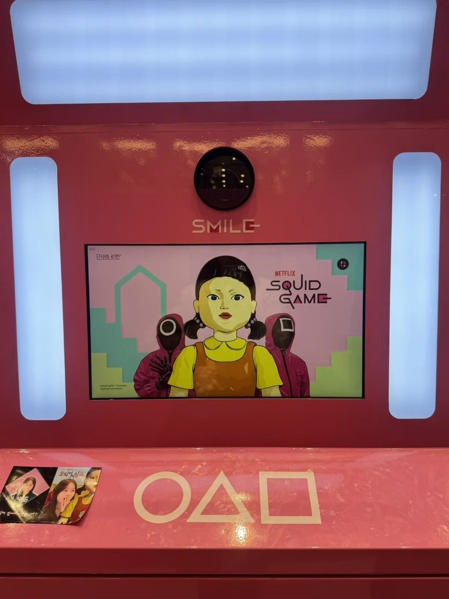 Cabina selfie rosa con immagini e simboli di Squid Game su schermo e superficie in Corea