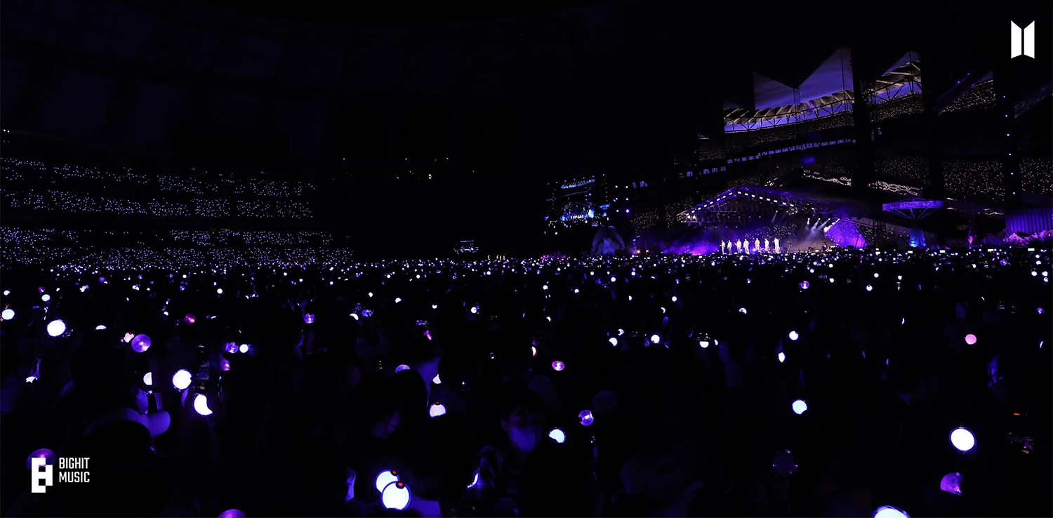 Foto di un concerto dei BTS visto dalla platea della fandom, con tantissime luci colare di azzurro-vilaceo.