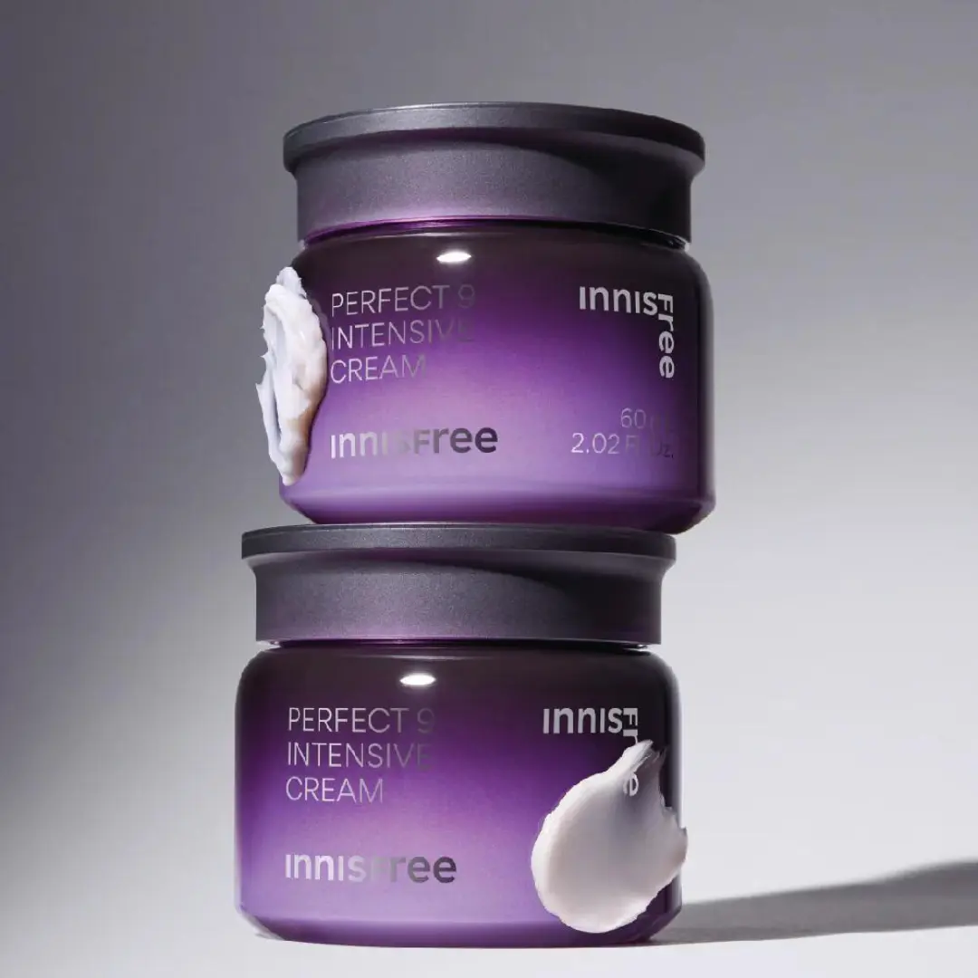 Due vasetti di Innisfree Perfect 9 Intensive Cream impilati, con packaging viola sfumato e texture della crema applicata sul bordo del contenitore.