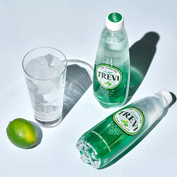 Immagine di due bottigliette dell'acqua coreana Trevi con un bicchiere con acqua e ghiaccio e un lime su sfondo celeste