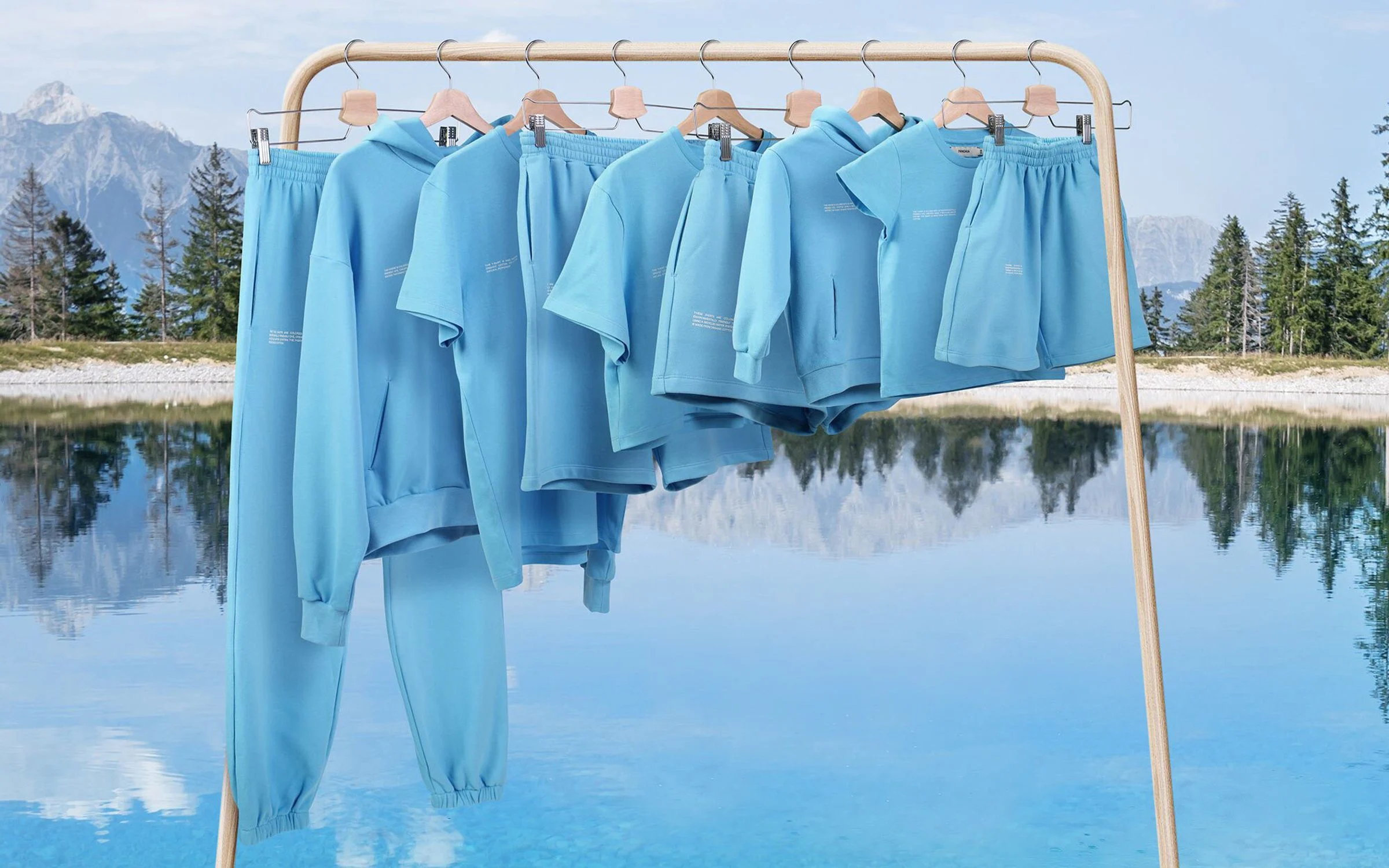 Abbigliamento Pangaia azzurro appeso a un appendiabiti con lago e montagne sullo sfondo.