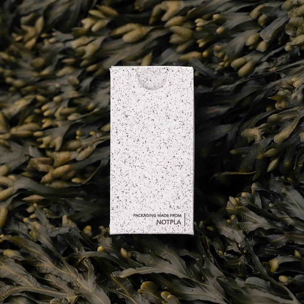 Scatola bianca Notpla realizzata con alghe biodegradabili, posata su sfondo di alghe marine naturali.