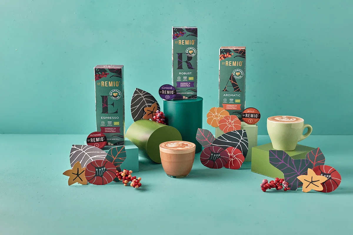 Confezioni St. Remio Caffee con cialde, cappuccini e decorazioni di carta su sfondo turchese Tre confezioni cialde St. Remio con gusti diversi, foglie e bacche di carta, cappuccini in vetro e tazza verde su sfondo turchese.