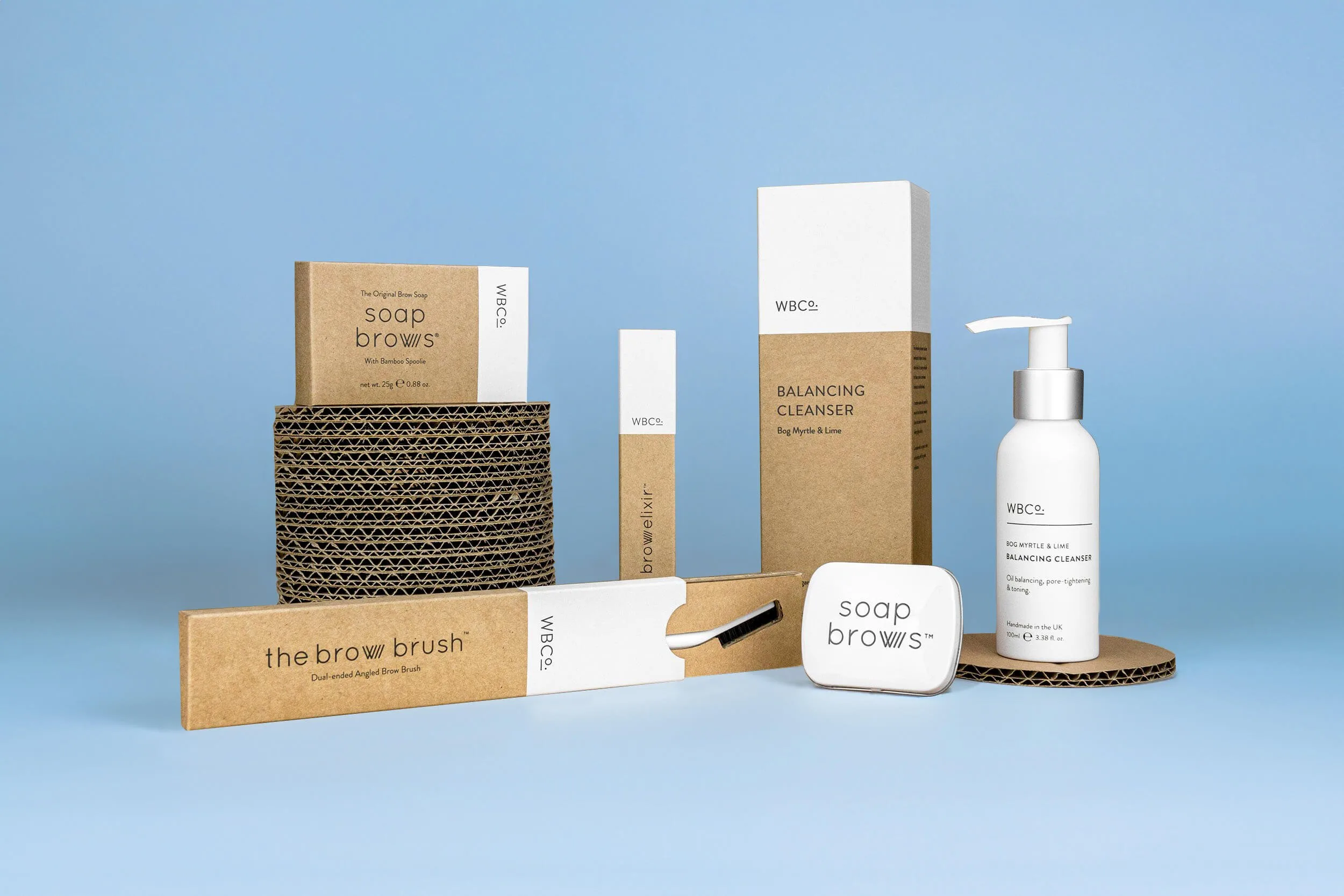 Packaging minimalista e sostenibile WBCO Clinic con scatola interna illustrata Prodotti WBCO Clinic con packaging bianco e cartone, scatola interna con immagine brow brush su sfondo azzurro.