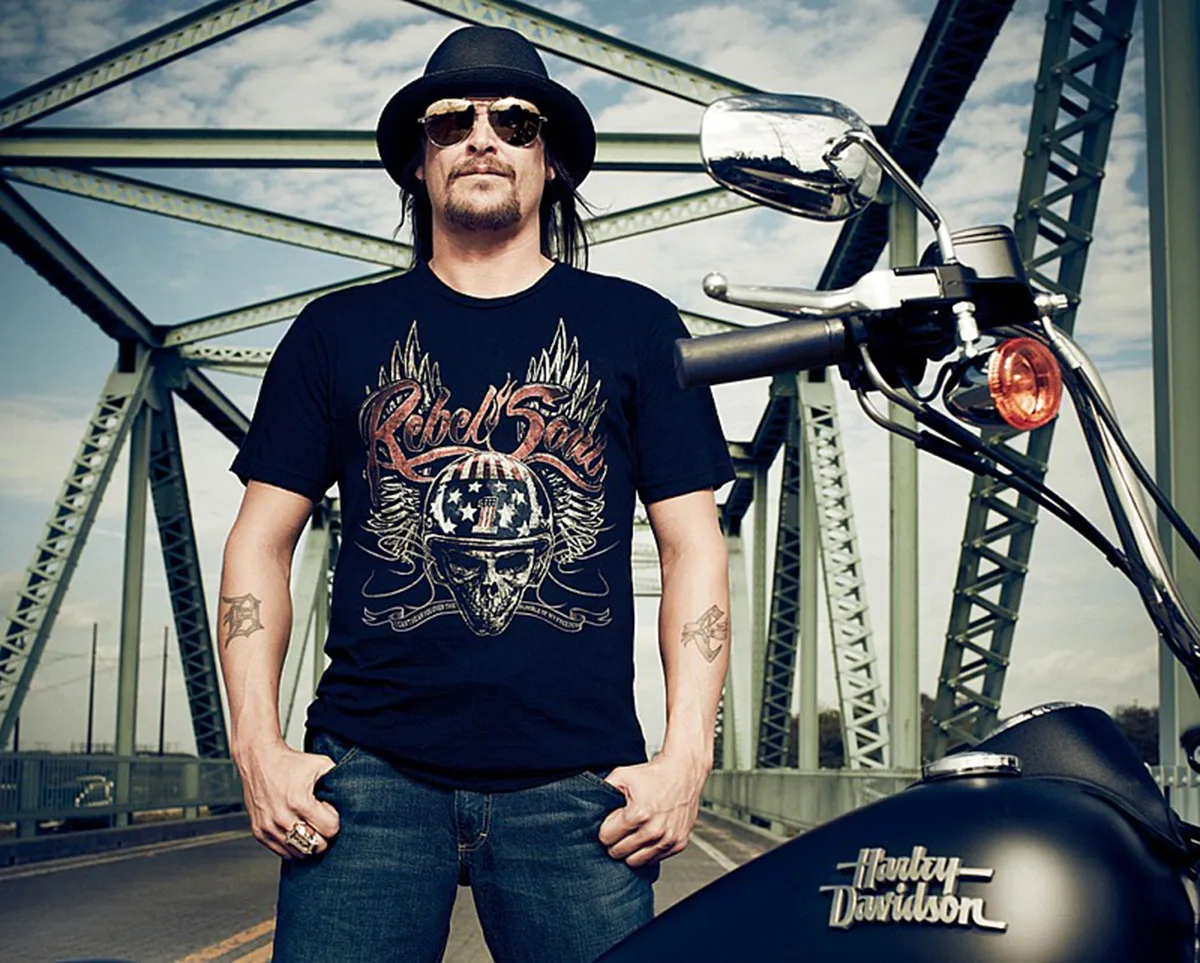 Kid Rock indossa una maglietta "Rebel Soul" e moto Harley-Davidson su un ponte in acciaio.