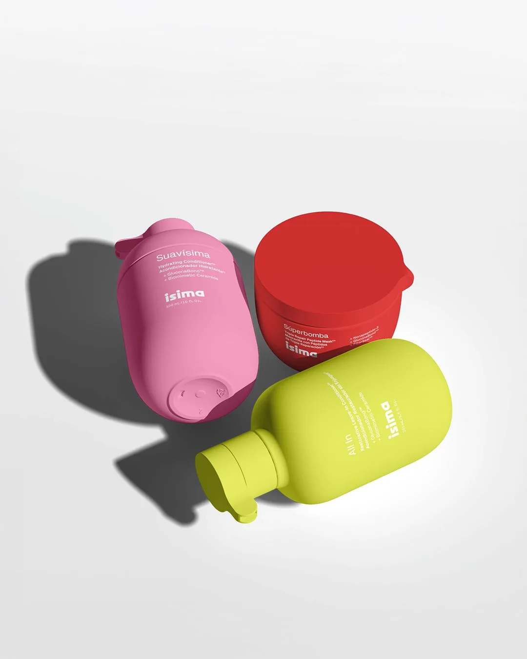 Tre prodotti della linea haircare Isima di Shakira. Rosa, verde acido e rosso.