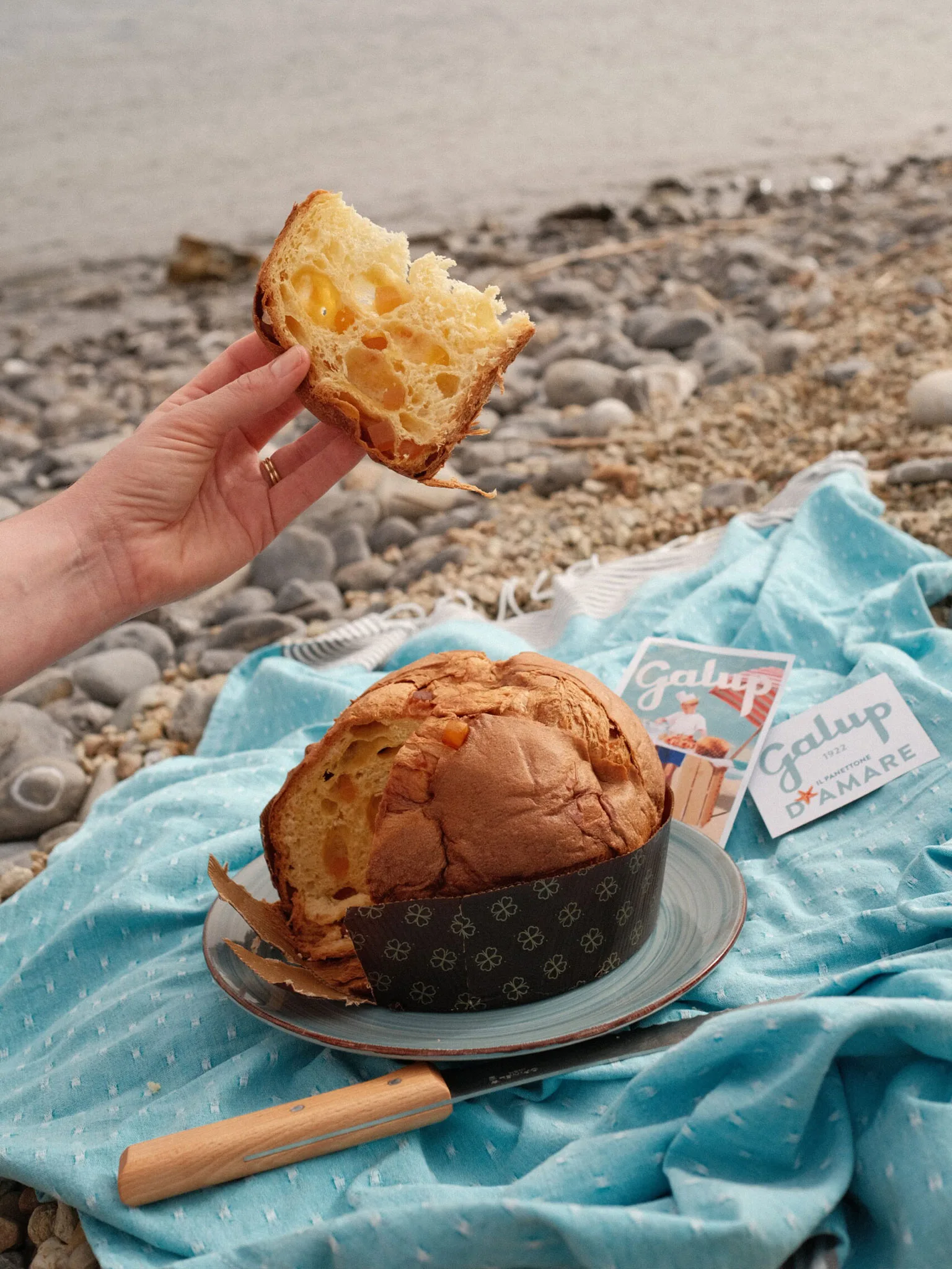 Fetta di panettone Galup gustata al mare su un telo azzurro tra i sassi della spiaggia.
