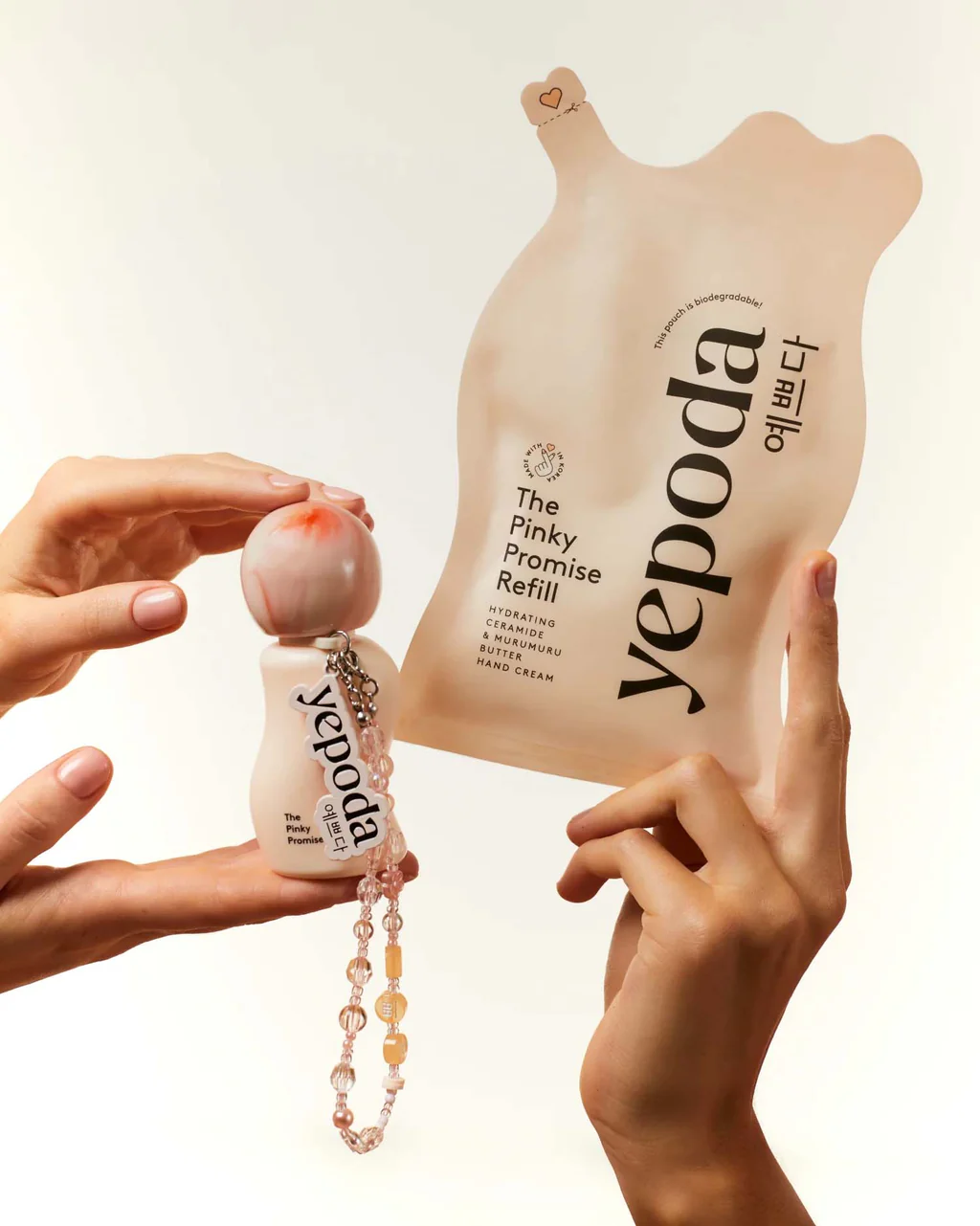 Mani mostrano la crema mani Yepoda The Pinky Promise con charm e la confezione refill, esempio di packaging indossabile.