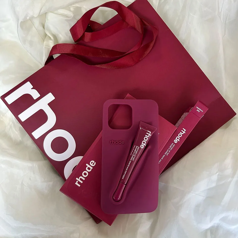 Custodia Rhode per smartphone con lipgloss abbinato, su shopper bordeaux dal design minimal.