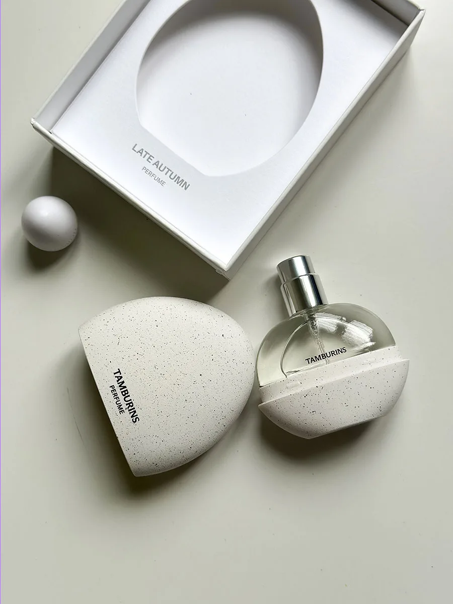 Profumo Tamburins “Late Autumn” con flacone rotondo e packaging minimal in pietra chiara, accanto alla confezione aperta.