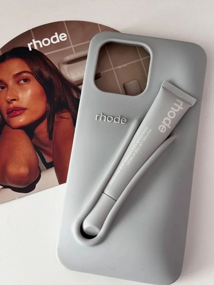 Kit Rhode con lip balm integrato in una custodia grigia da smartphone, accanto a foto di campagna con Hailey Bieber.