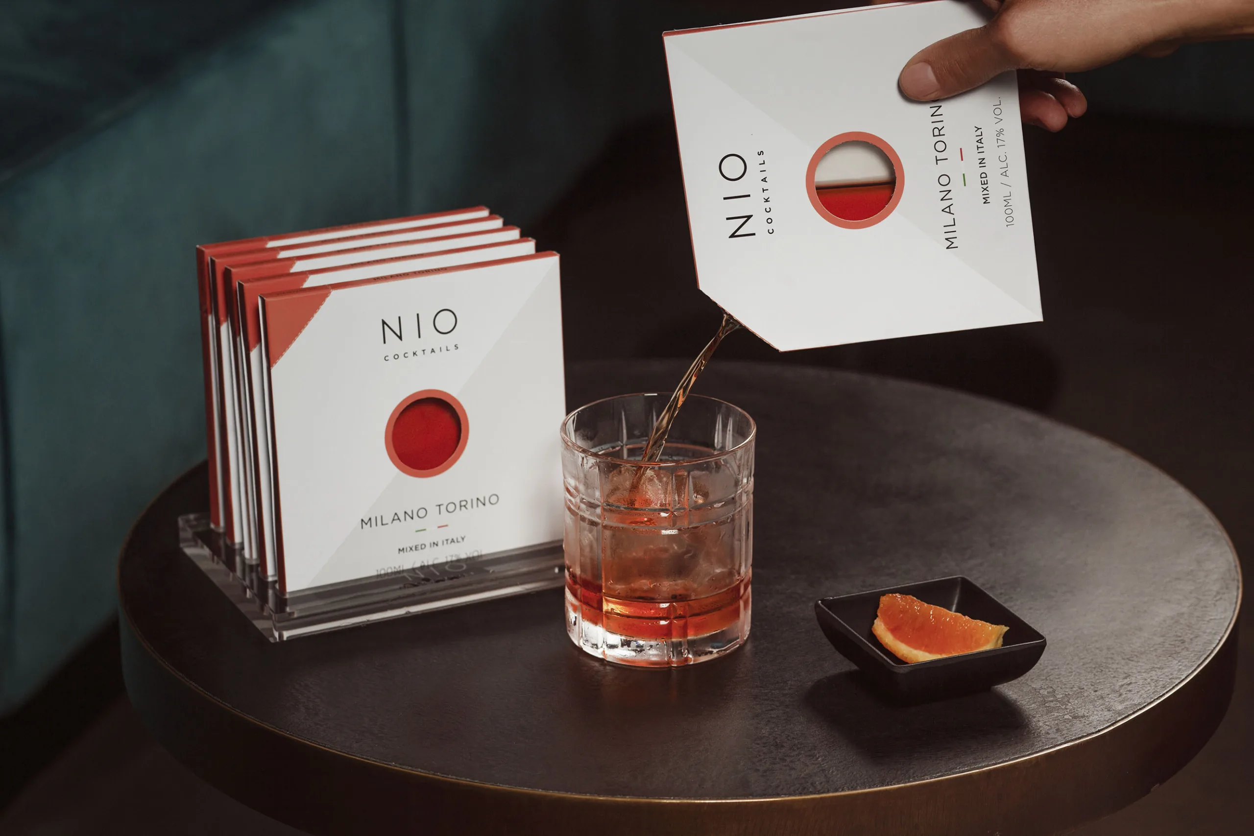 Confezioni di NIO Cocktails Milano-Torino con bicchiere e fetta d'arancia su tavolo di legno