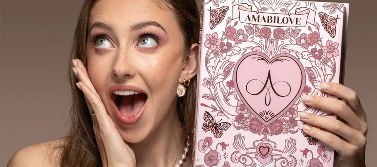 Martina Strazzer sorride sorpresa tenendo il catalogo rosa Amabilove con logo e decorazioni floreali