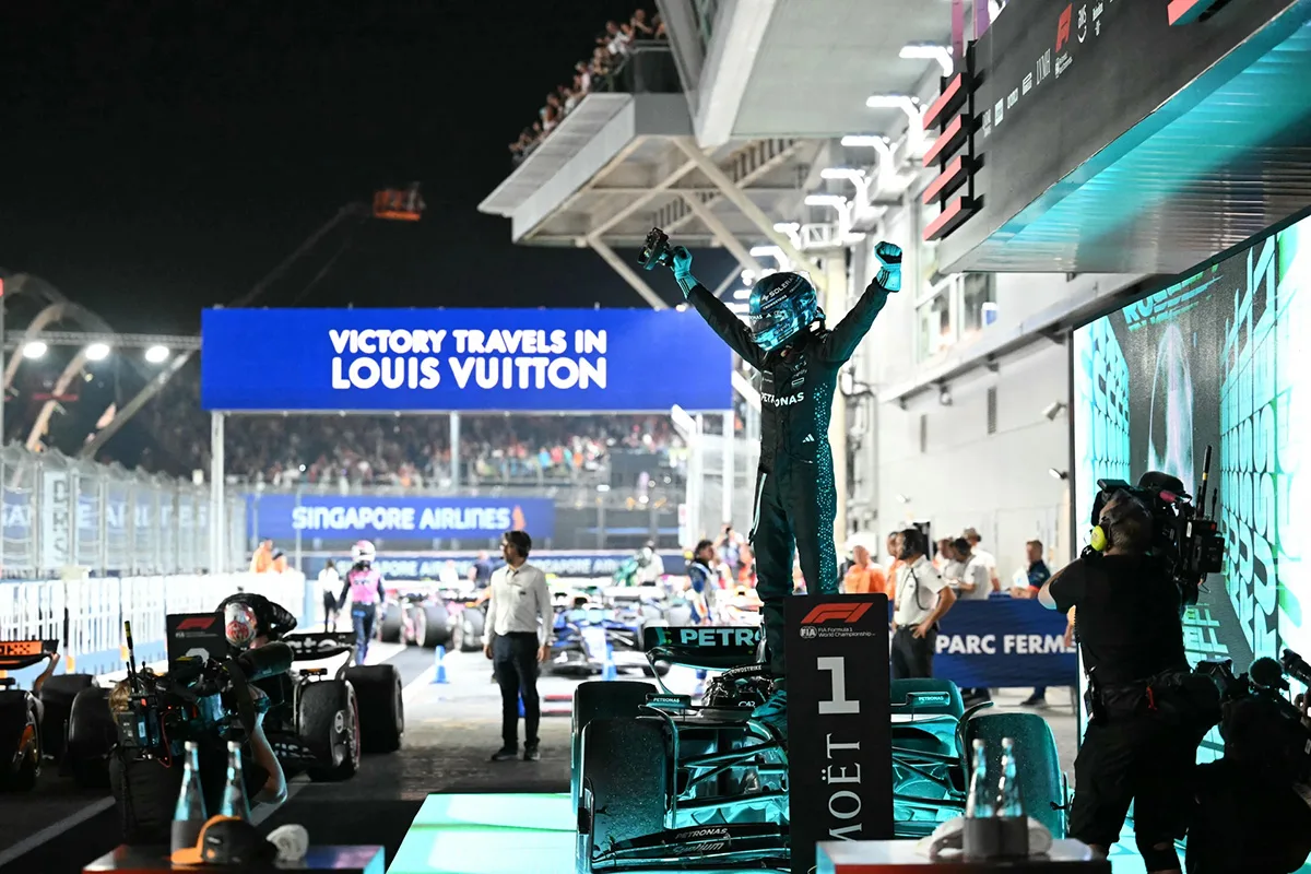 Pilota Mercedes F1 esulta a Singapore dopo la vittoria, esempio di F1 experiential marketing con spazio Louis Vuitton e Moët sullo sfondo.